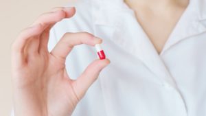 infermiere që demonstron pilulë të vogël me dy ngjyra
